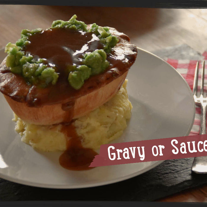 Hot pie served on a plate sitting on top of mashed potato and topped with mushy peas and gravy