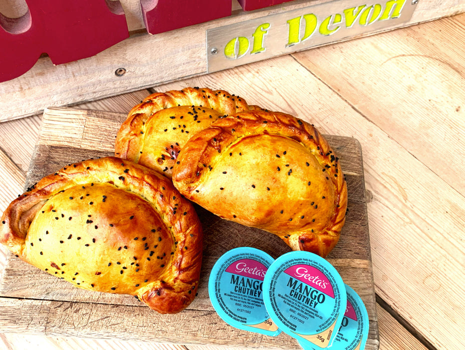 Three butter chicken curry pasties on a wood cutting board with three packs of geetas mango chutney.