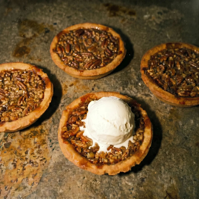 Pecan tarts on a rustic surface with one topped with ice cream.