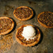 Pecan tarts on a rustic surface with one topped with ice cream.
