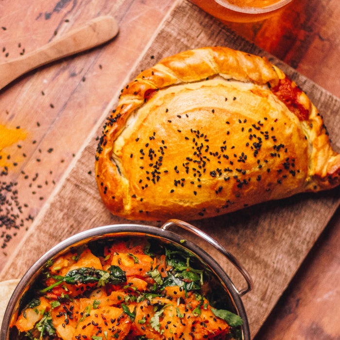 Chunk Original Butter Chicken Curry pasty served on a wooden board with an Indian side dish and mango chutney.
