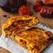 Chunk Chicken & Chorizo pasty one half on top of the other on served on a wooden cutting board, with chunks of Spanish chorizo and a glass of red wine.