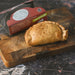 Chunk original baked steak and blue cheese pasty on a wooden cutting board.