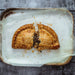 Chunk original Steak pasty, baked on a baking tray, cut in half with filling spilling out, on a rustic metal surface.