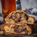 Chunk original steak pasty baked then cut in half to reveal an award winning filling. A knife holds the two halves together.