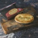 A baked Chunk chicken, mushroom & tarragon pie sits on a wooden cutting board next to its branded cardboard packaging box.