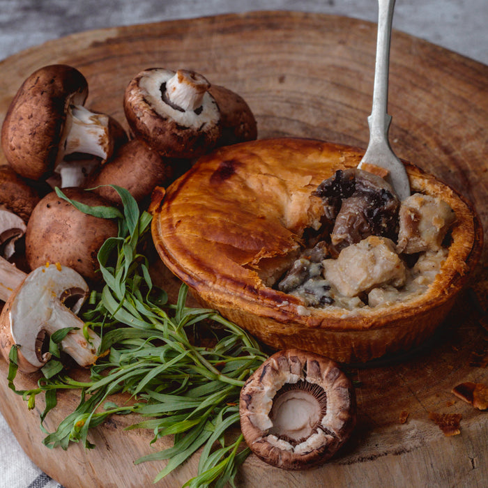Chunk Chicken, Mushroom & Tarragon pie on a wooden board with fresh mushrooms and herbs.