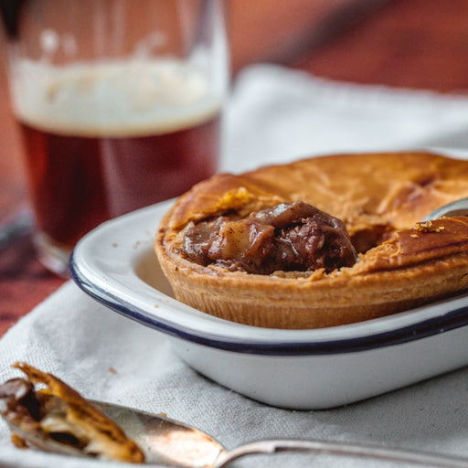 Chunk Steak Pie on a white plate with a glass of beer in the background.

