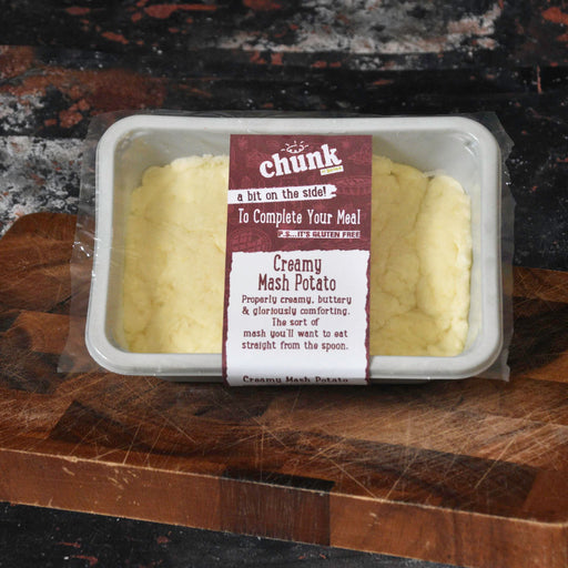 A packaged tray of creamy mash potato with a visible front label reading 'chunk' and 'Creamy Mash Potato,' placed on a wooden cutting board over a dark countertop.