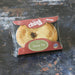 A packaged round baked good labeled 'Chunk Original Sheep Pie' in clear plastic with red and green packaging, placed on a dark rustic surface.