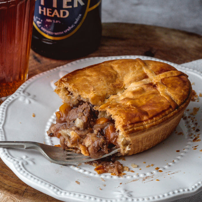 Chunk Original Steak & Ale Pie on a plate with a fork, glass of beer, and bottle of ale in the background.