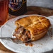 Chunk Original Steak & Ale Pie on a plate with a fork, glass of beer, and bottle of ale in the background.