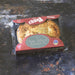 A packaged meat pie from Chunk Original, showing the cooked pie through clear plastic packaging with a red cardboard header, placed on a dark rustic surface.
