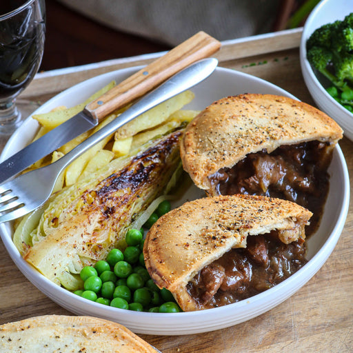Meat pie with sides of chips, peas, and a glass of wine on a wooden table.