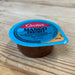 A small Geeta's Mango Chutney container with a bright blue lid sits on a light wood grain surface.